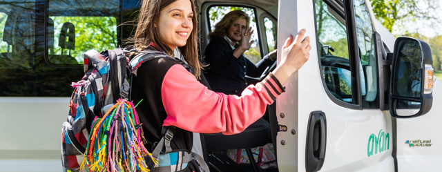 Meisje staat op het punt om de deur dicht te doen na het uitstappen, op de achtergrond zwaait de chauffeur naar haar.