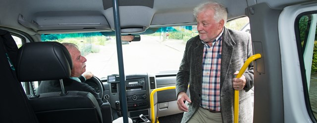 Een oudere man stapt voorin een Avan-bus en begroet de chauffeur.