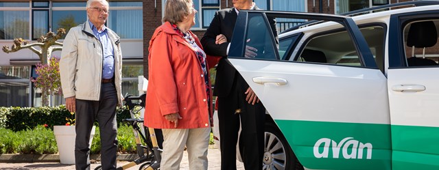 Een chauffeur helpt een vrouw met instappen in een Avan personenauto.