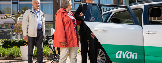 Een chauffeur helpt een vrouw met instappen in een Avan personenauto.